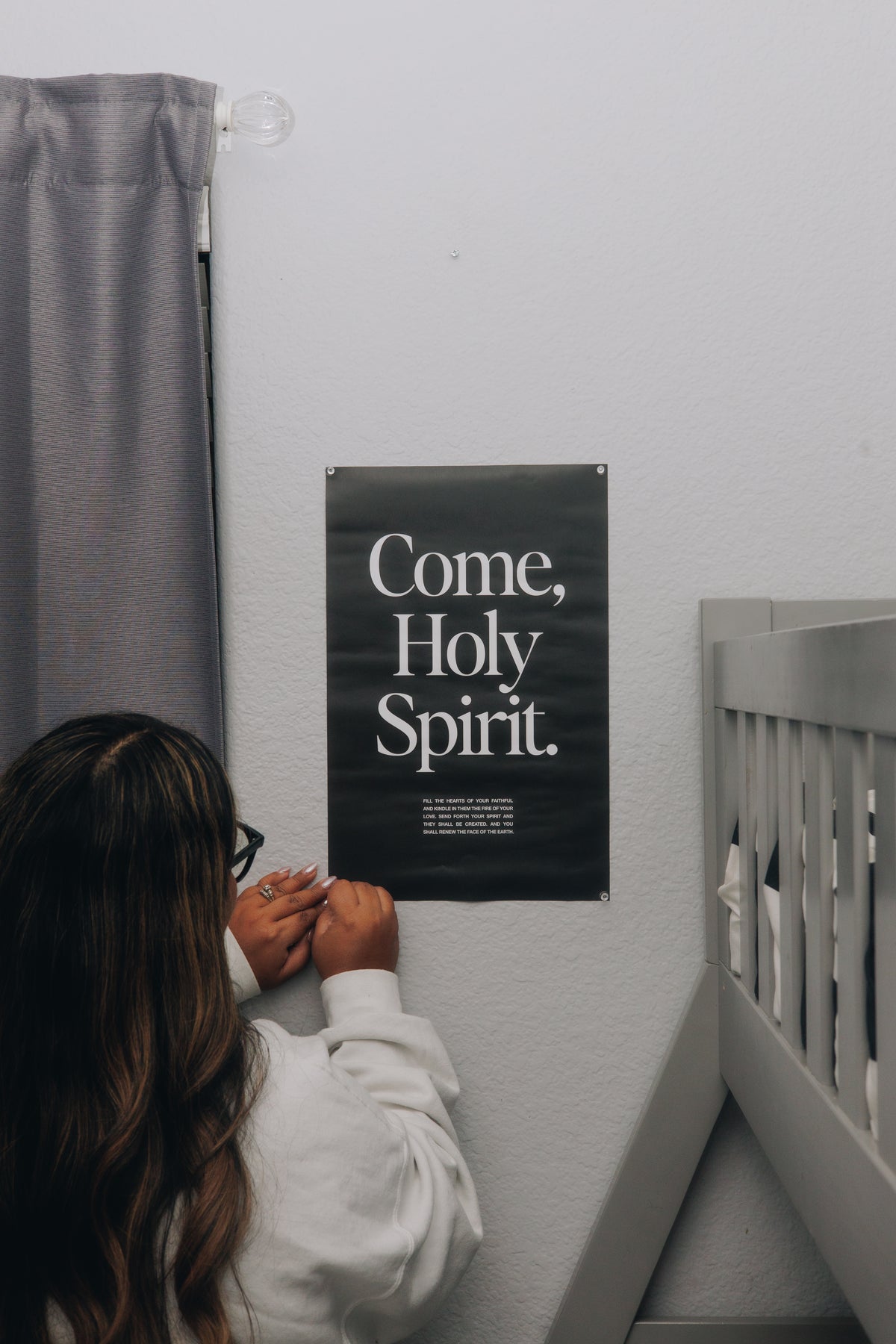 Woman viewing a peaceful Come Holy Spirit prayer print displayed beside a crib, creating a faith filled reminder of God’s presence in the home